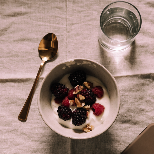A bowl of Greek yogurt with berries and walnuts on a linen tablecloth