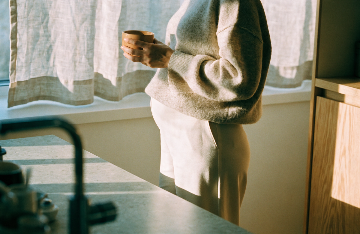 An expectant mother standing calmly at a sunlit kitchen counter with a warm mug